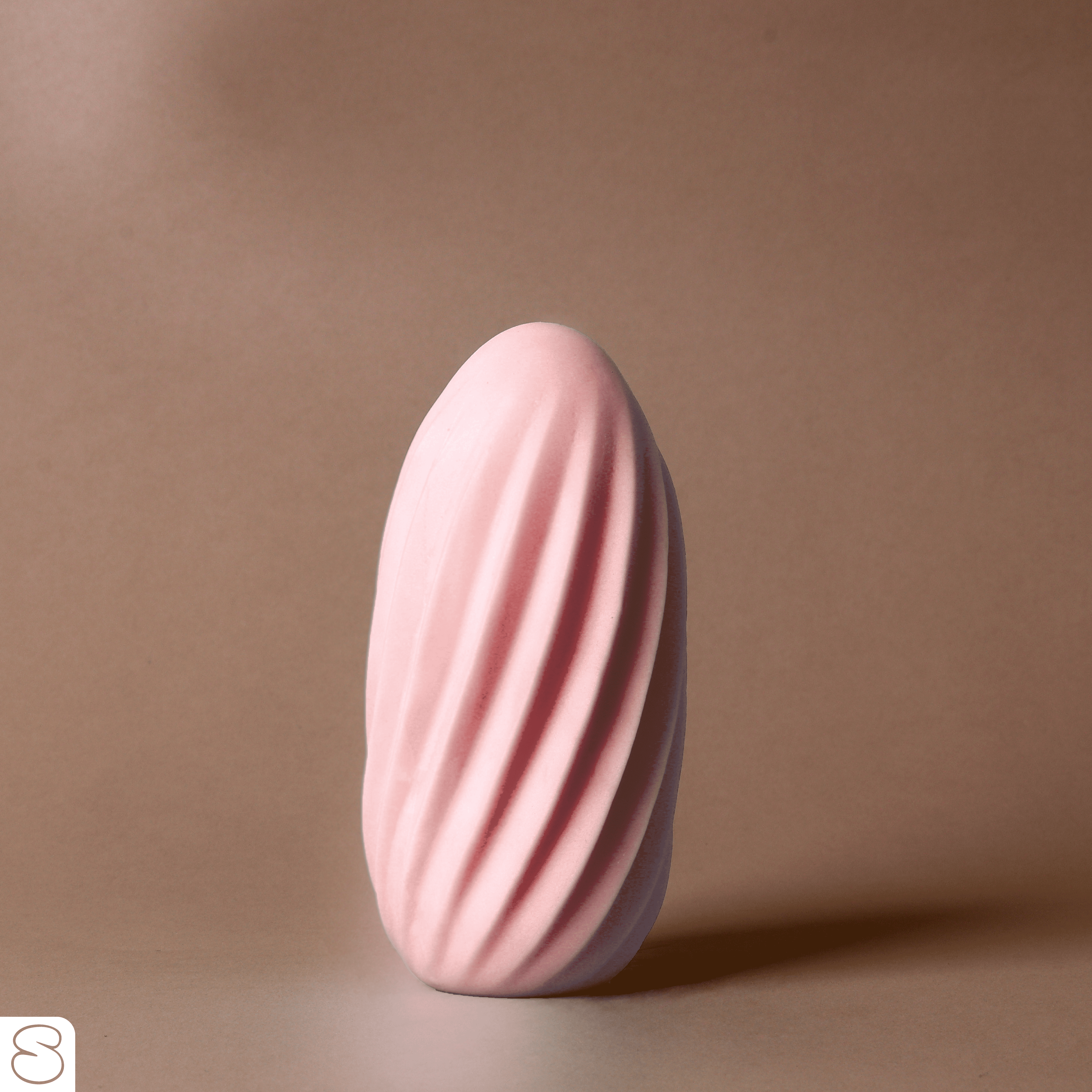 Soft pink ribbed massager standing upright on a warm-toned background, shot in natural light