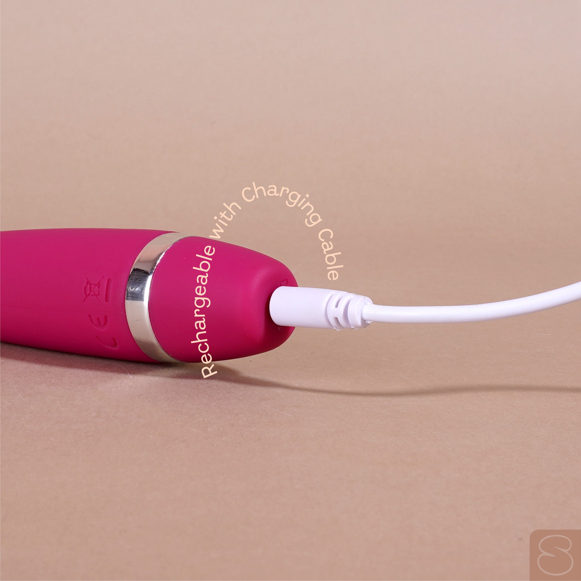 Close-up of pink massager being charged with white cable on beige background