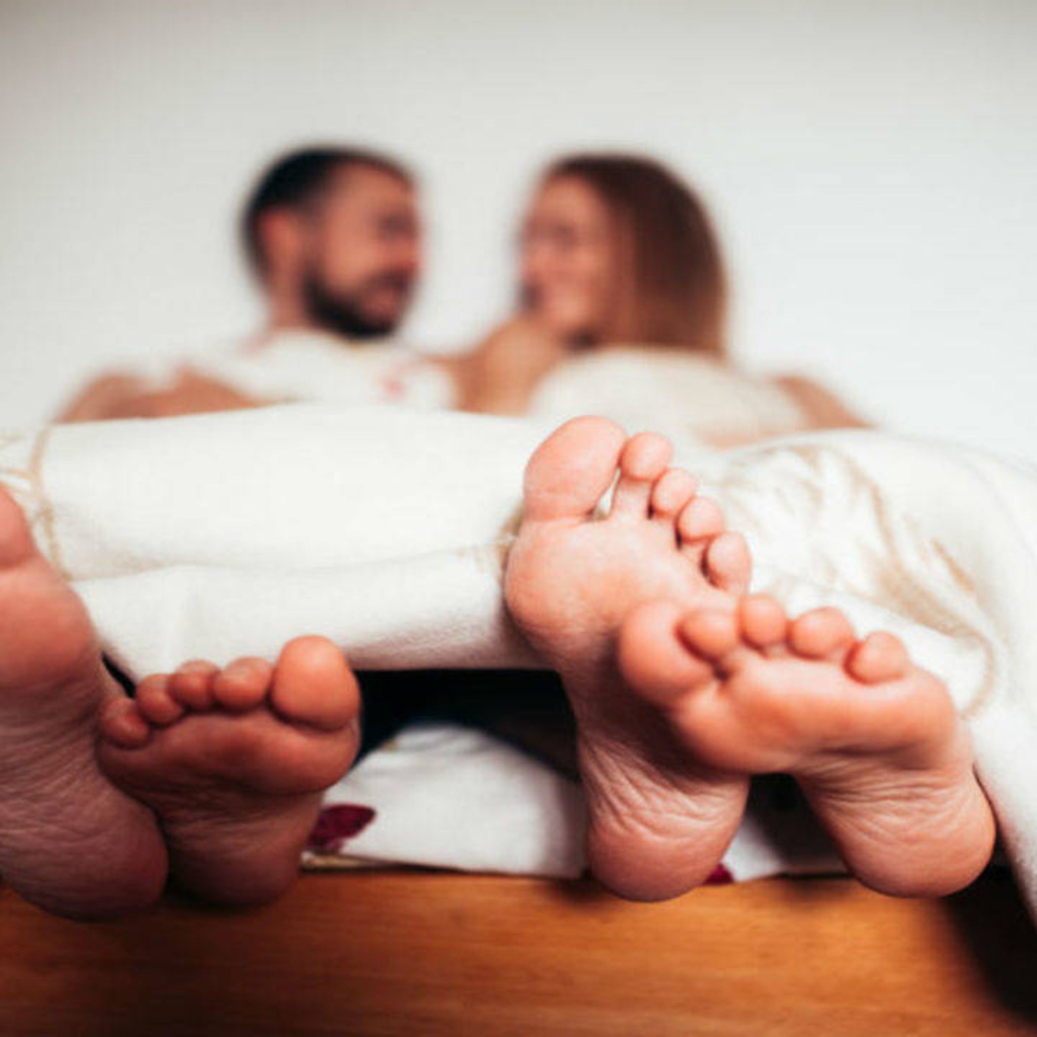 How to know if a guy is a virgin – A blurred couple in bed with their feet visible under the covers, symbolizing intimacy and relationships.