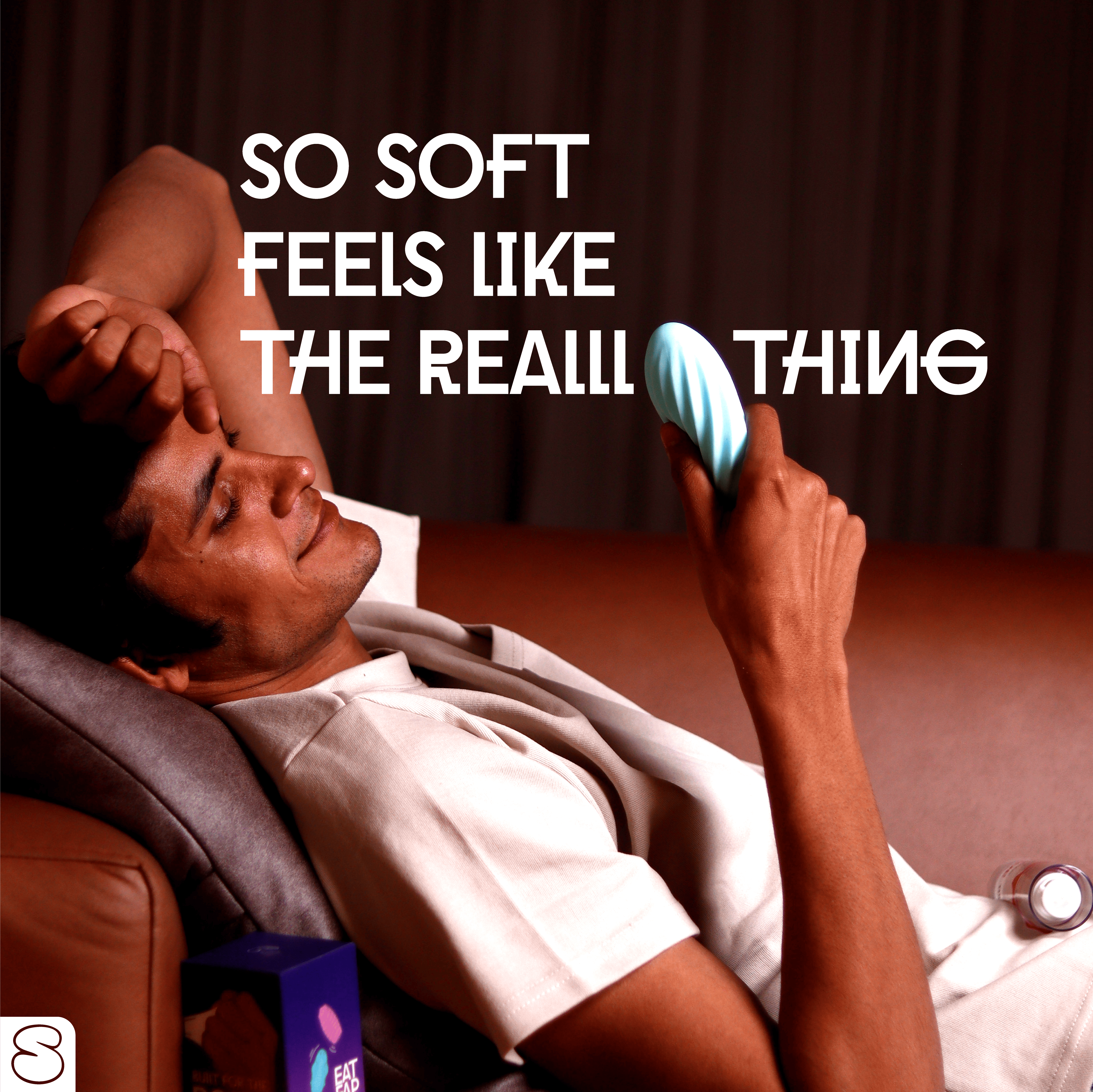 Man relaxing on couch holding soft blue silicone stroker with a happy expression