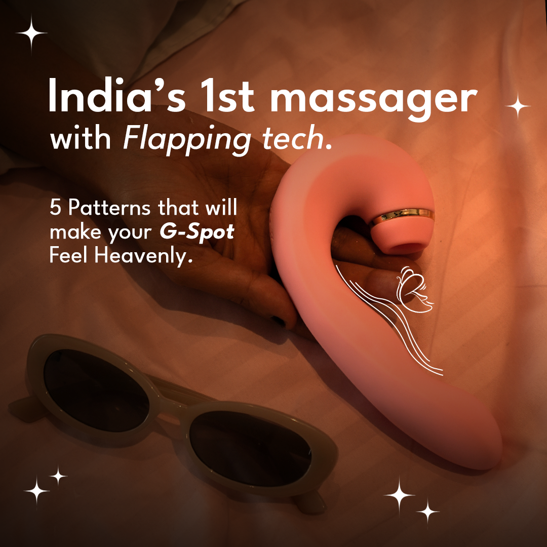 Hand holding a curved pink massager with gold detailing and sunglasses on satin fabric